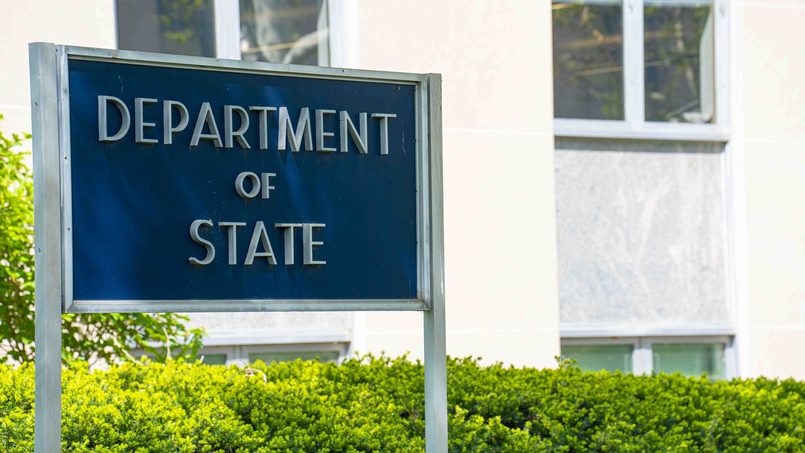 Blue Department of State sign outside the Harry S. Truman Building in Washington, with hedges in front
