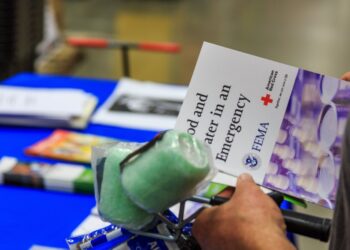 A shopper holds a FEMA and American Red Cross brochure titled Food and Water in an Emergency at a preparedness display in a hardware store