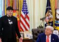 Elon Musk stands and speaks beside President Donald Trump, seated at the Resolute Desk in the Oval Office