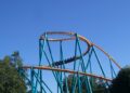 The orange track and teal supports of the Goliath roller coaster at Six Flags Over Georgia, with a train passing through a helix against a blue sky