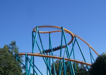 The orange track and teal supports of the Goliath roller coaster at Six Flags Over Georgia, with a train passing through a helix against a blue sky