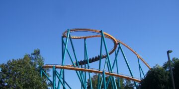 The orange track and teal supports of the Goliath roller coaster at Six Flags Over Georgia, with a train passing through a helix against a blue sky