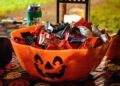 An orange jack-o'-lantern bowl filled with fun-size chocolate bars set out for trick-or-treaters at night
