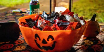 An orange jack-o'-lantern bowl filled with fun-size chocolate bars set out for trick-or-treaters at night