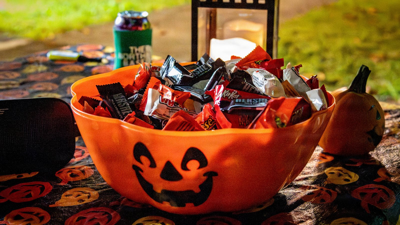 An orange jack-o'-lantern bowl filled with fun-size chocolate bars set out for trick-or-treaters at night