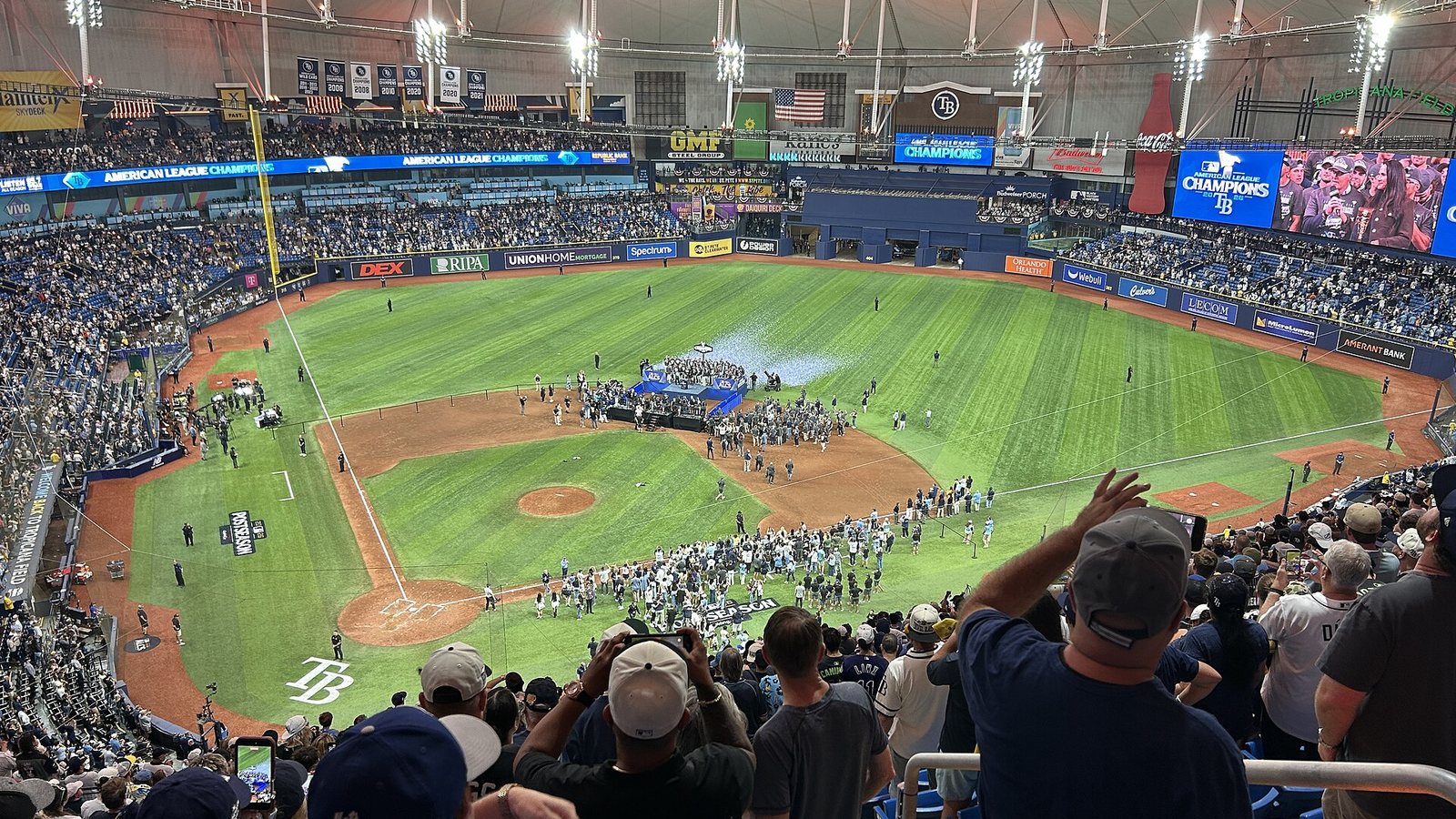Fans in the upper deck at Tropicana Field watch the Rays' American League championship trophy ceremony on the infield, with American League Champions graphics on the stadium video boards