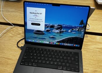 An open 14-inch MacBook Pro in Space Black on a wooden store display table, its screen showing the camera notch at the top