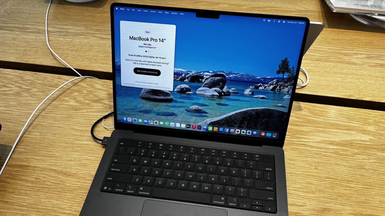 An open 14-inch MacBook Pro in Space Black on a wooden store display table, its screen showing the camera notch at the top