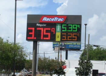 A RaceTrac gas station sign listing prices for regular gasoline, diesel and E85, with trees and power lines below