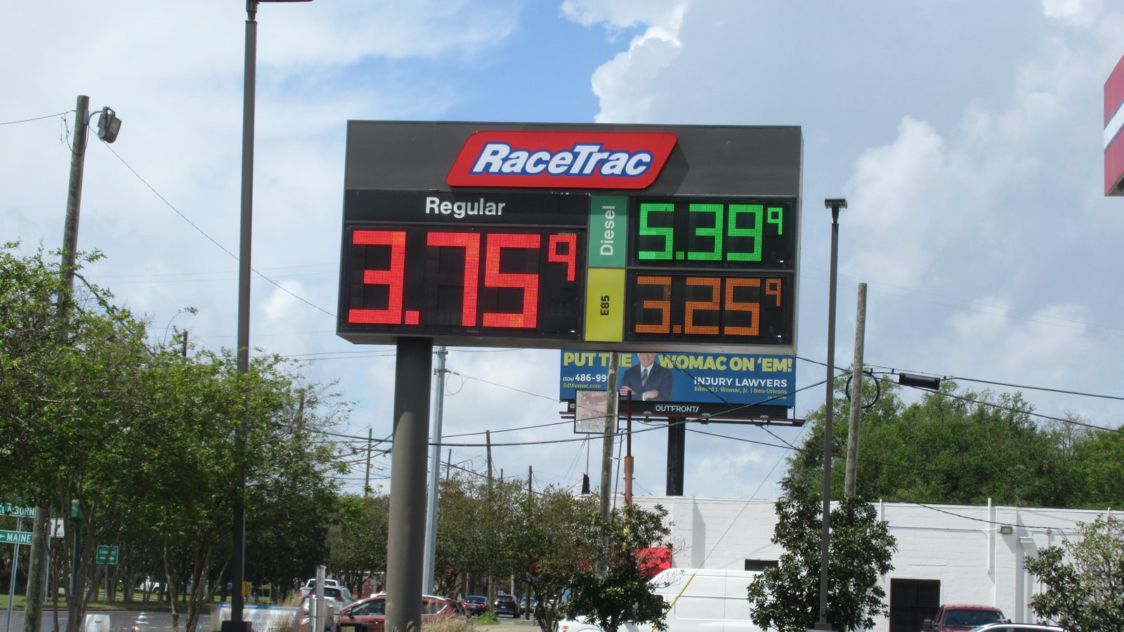 A RaceTrac gas station sign listing prices for regular gasoline, diesel and E85, with trees and power lines below