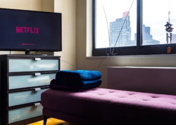 A TV showing the Netflix logo on a dresser in an empty living room beside a purple bench and a window overlooking city buildings
