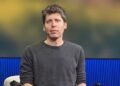 OpenAI chief executive Sam Altman, in a gray sweater, seated on the TED stage in front of a blue and gold backdrop
