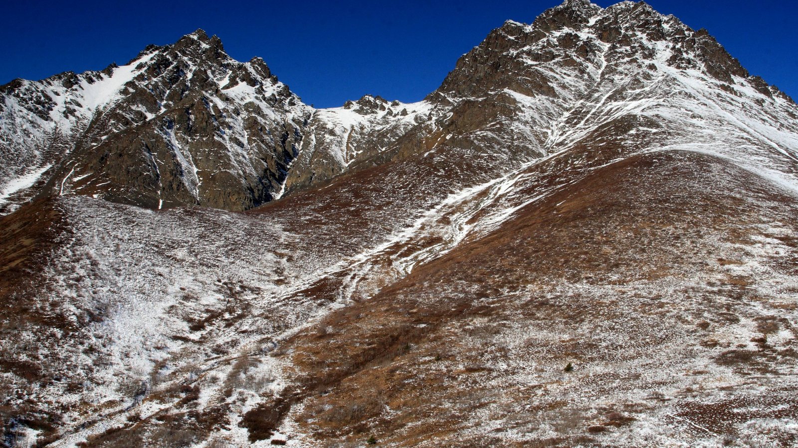 Rocky mountain slopes lightly dusted with early-season snow under a deep blue sky at Twin Peaks above Eklutna Lake, Alaska