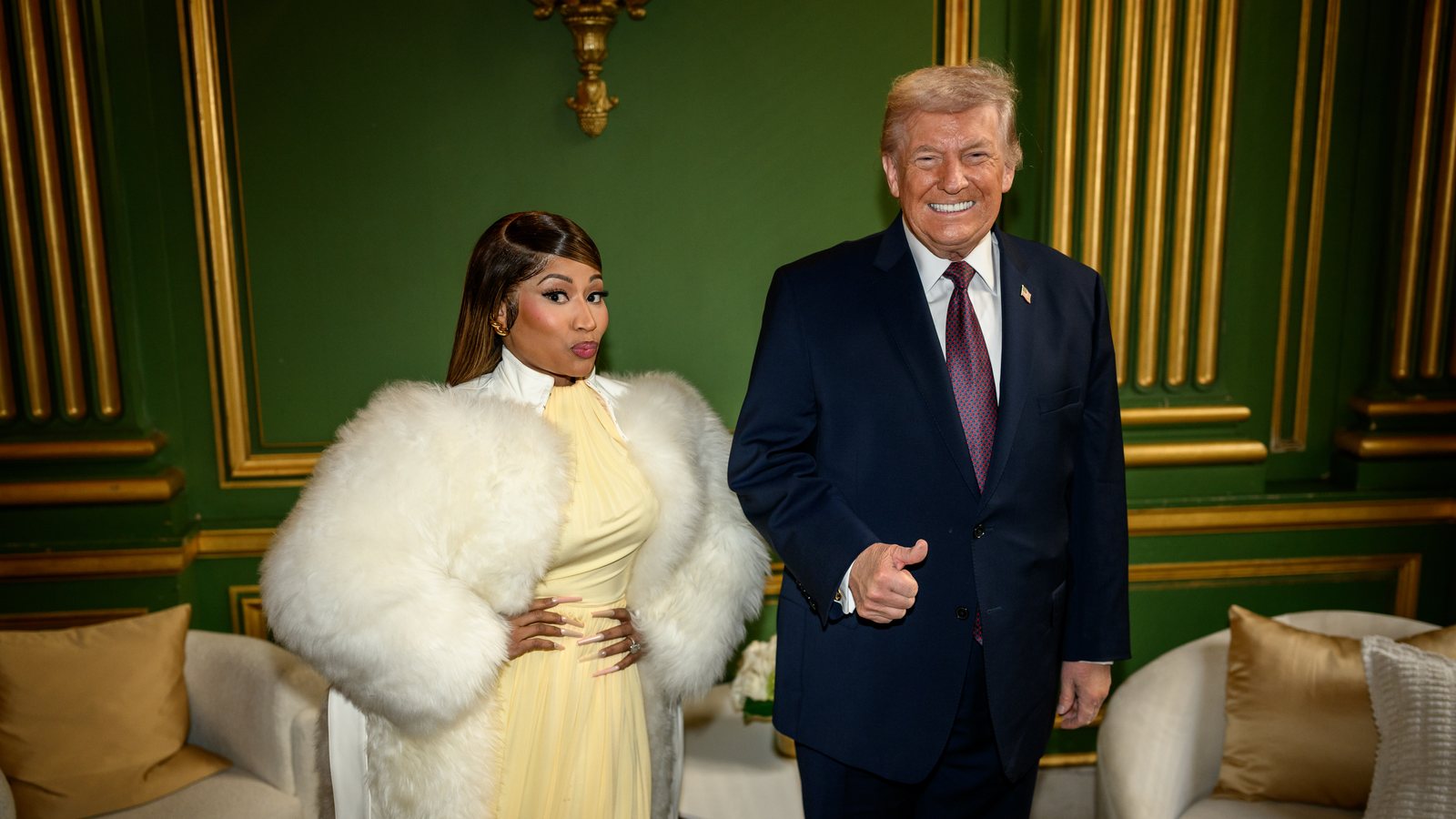 Nicki Minaj, in a white fur coat and yellow dress, stands beside President Donald Trump, who gives a thumbs-up, in a green-panelled room