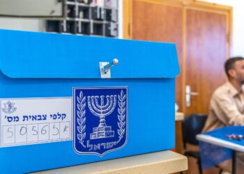 A blue Israeli ballot box with the state emblem and a numbered label on a counter at a military polling station