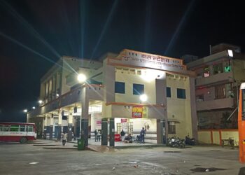 The Uttar Pradesh state bus station in Mau, India, lit up at night with a red bus parked outside