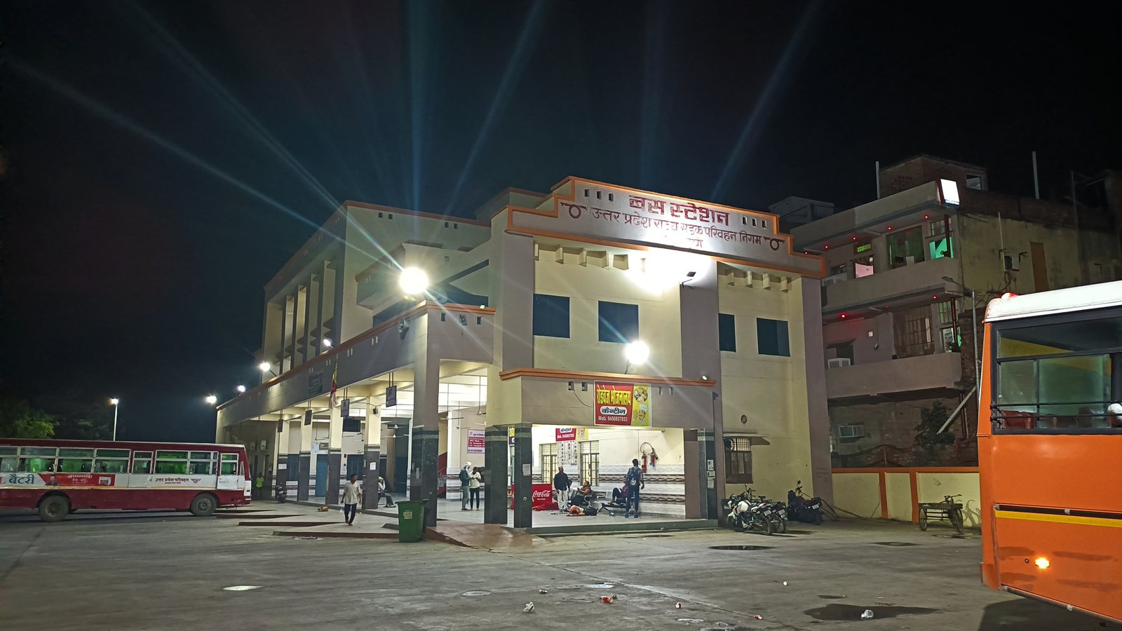 The Uttar Pradesh state bus station in Mau, India, lit up at night with a red bus parked outside