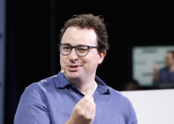 Anthropic CEO Dario Amodei, wearing glasses and a blue shirt, speaks on stage at TechCrunch Disrupt in 2023