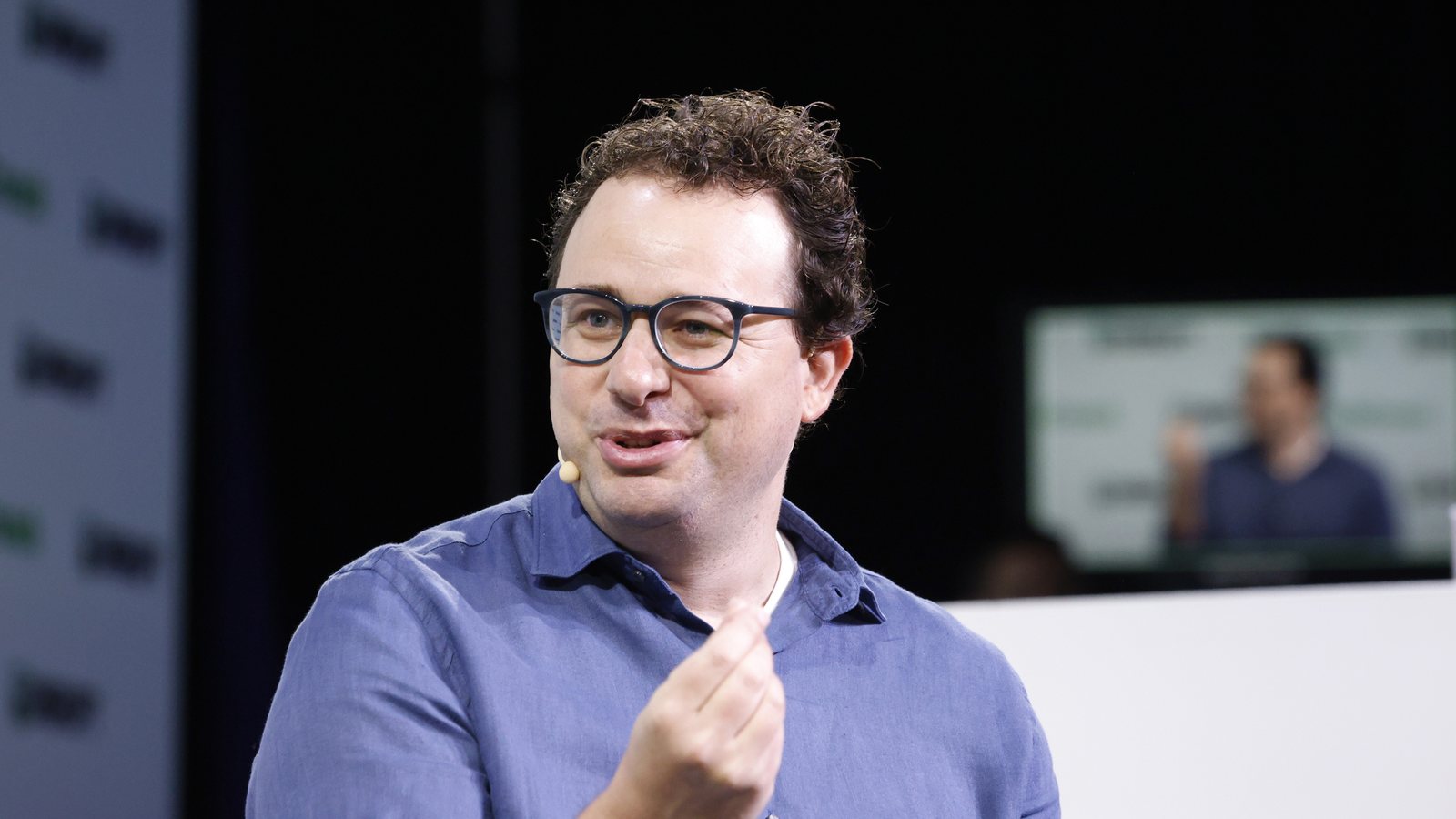 Anthropic CEO Dario Amodei, wearing glasses and a blue shirt, speaks on stage at TechCrunch Disrupt in 2023