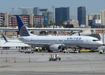 A white United Airlines Boeing 737 with a blue globe tail parked at a gate at the Las Vegas airport, with Strip hotel towers behind it